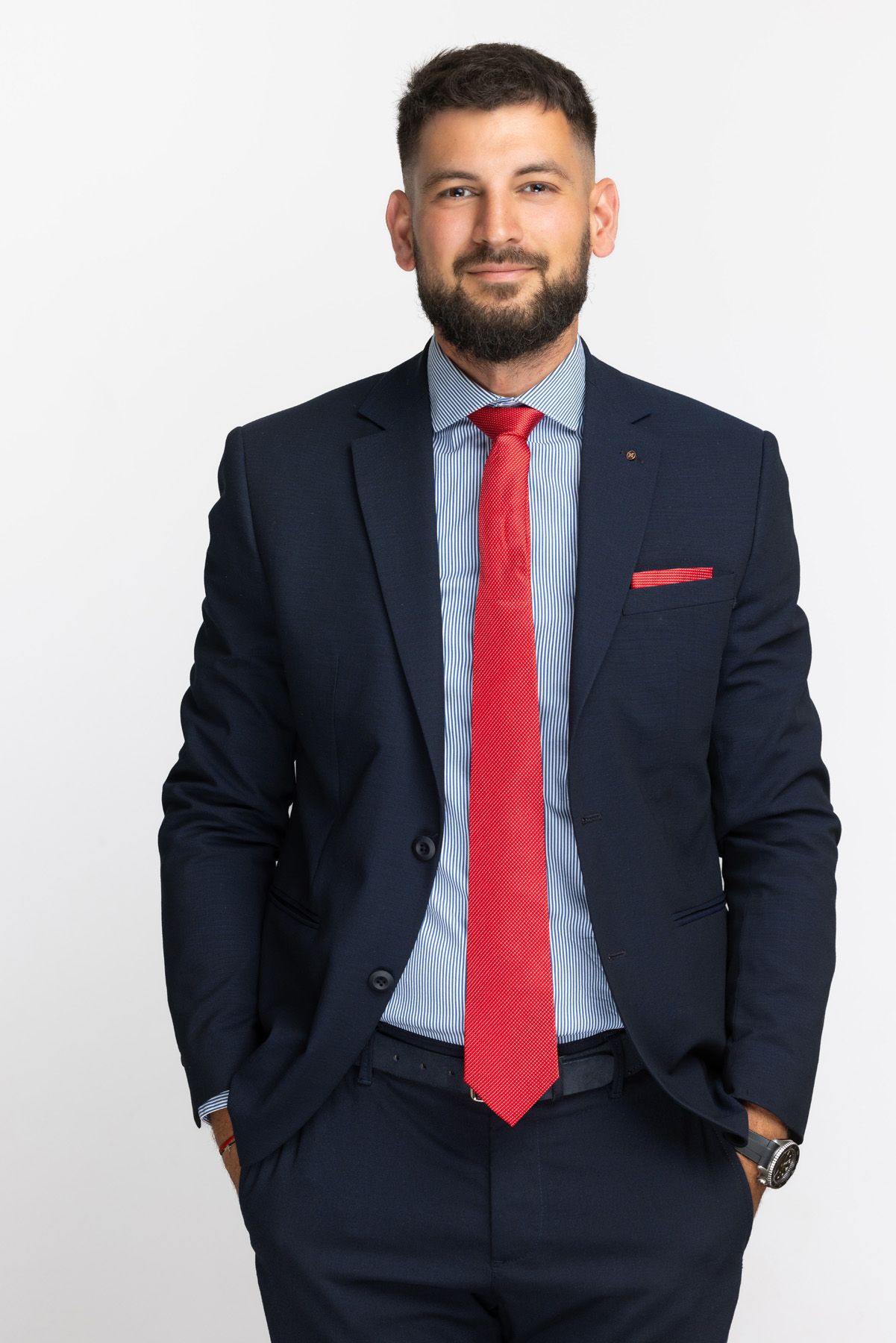 Professional portrait of person in navy suit with bright red tie and pocket square against white background.