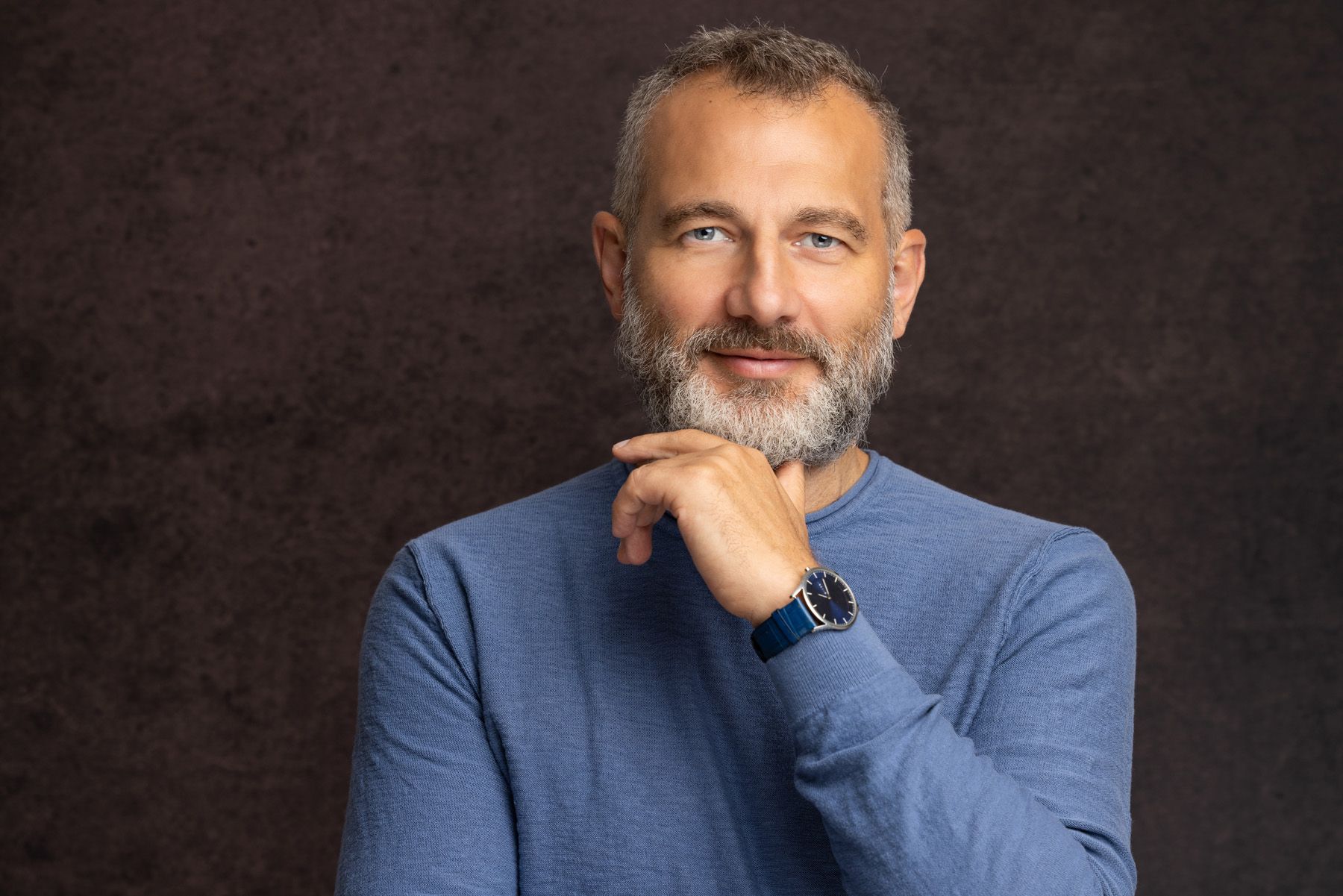 Professional portrait headshots of a person in a navy blue sweater against a dark background.