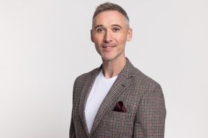 Professional portrait of man wearing checkered blazer and white shirt against light backdrop.