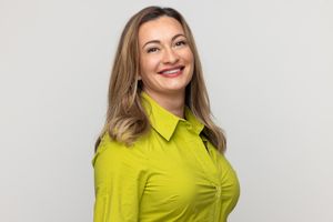 Professional headshot of woman in lime green button-up blouse against white background.