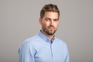 Professional portrait of person wearing light blue button-down shirt against gray background.