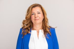 Professional portrait of person in royal blue blazer and white blouse against neutral background.