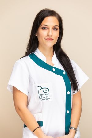 Healthcare professional wearing a white uniform with teal accents and an embroidered logo standing against beige background.
