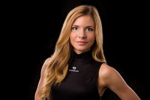 Headshot portrait of a person with blonde hair wearing a black sleeveless turtleneck against dark background.