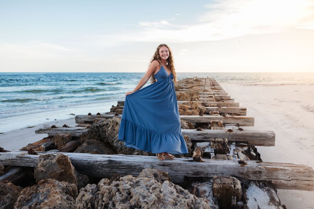 Sunset photoshoot at the beach shows a flowing blue dress against golden light and breaking waves.