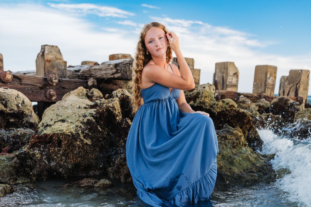 Coastal photoshoot featuring a blue dress against rocky shoreline and ocean waves.