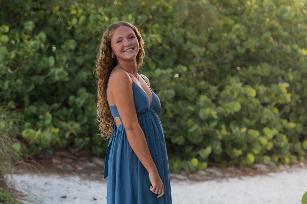 A flowing blue sundress is showcased against lush green foliage and white sandy beach background.