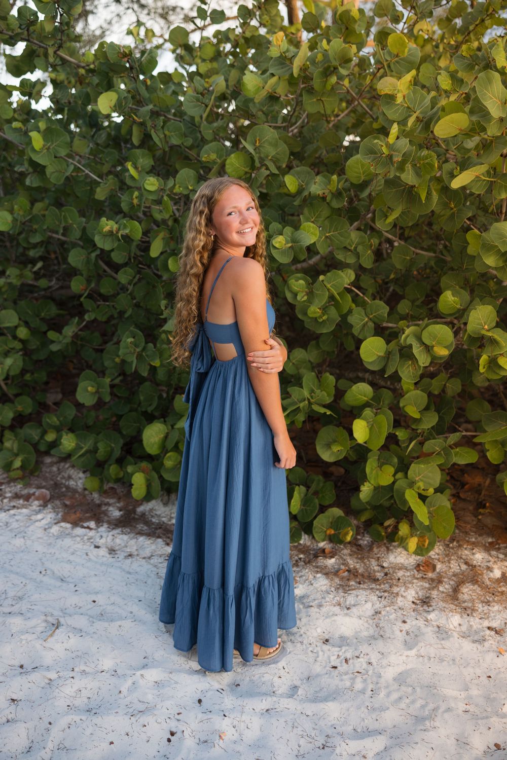 Multiple poses in a blue flowing maxi dress against tropical greenery and white sand.
