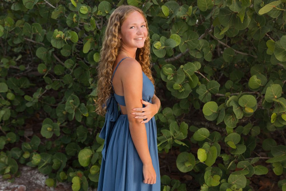 A series of beachside poses featuring a flowing blue dress against green foliage.