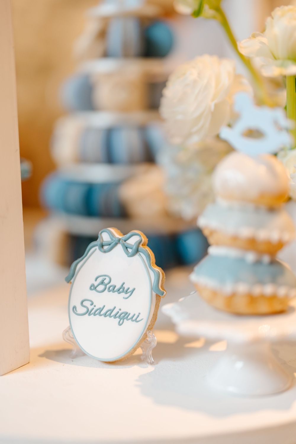 Custom decorated baby shower cookie reading Baby Siddiqui in blue lettering with bow design.