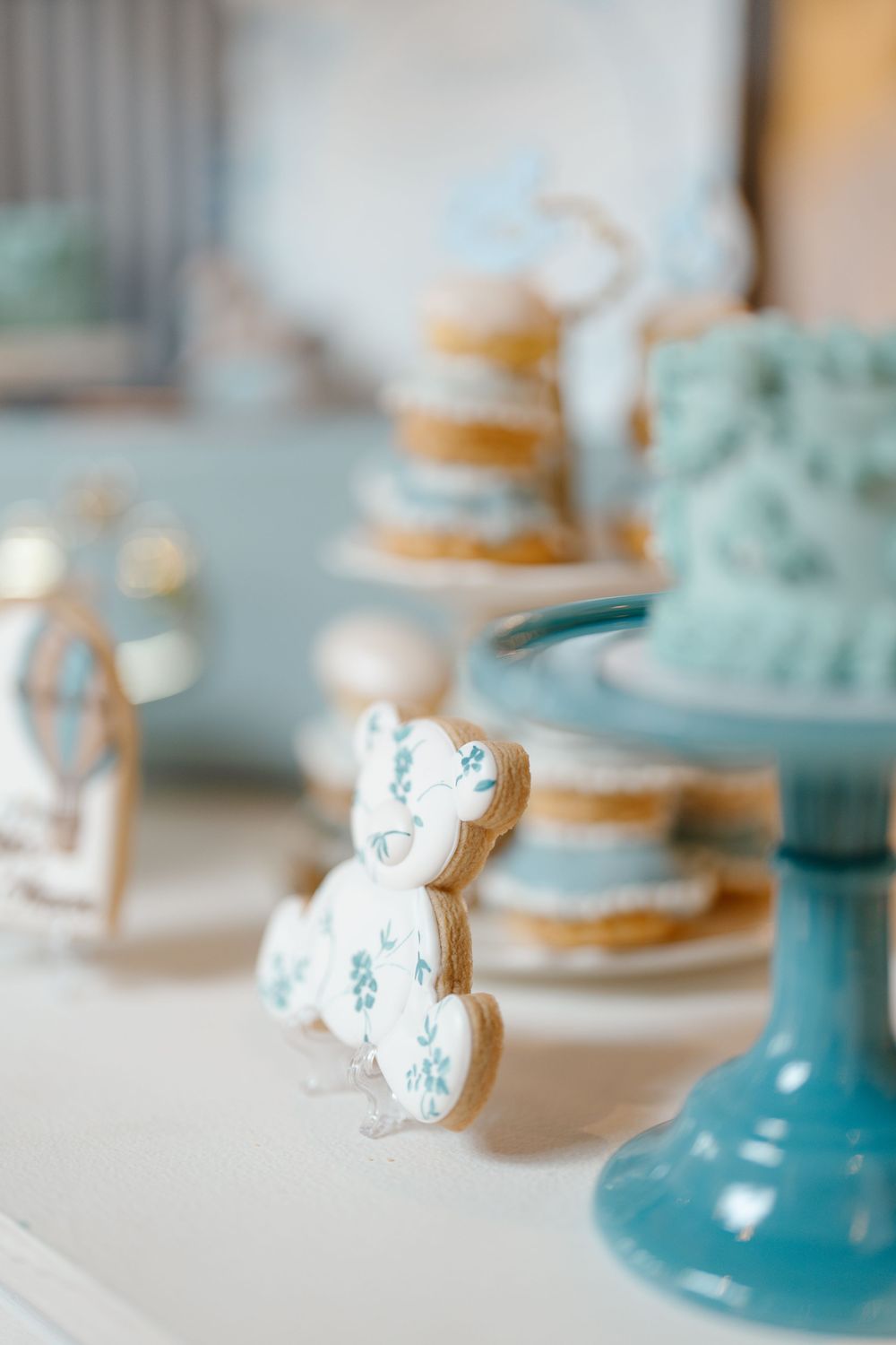 Blue and white teddy bear shaped cookies displayed near a mint cake stand at a baby shower.