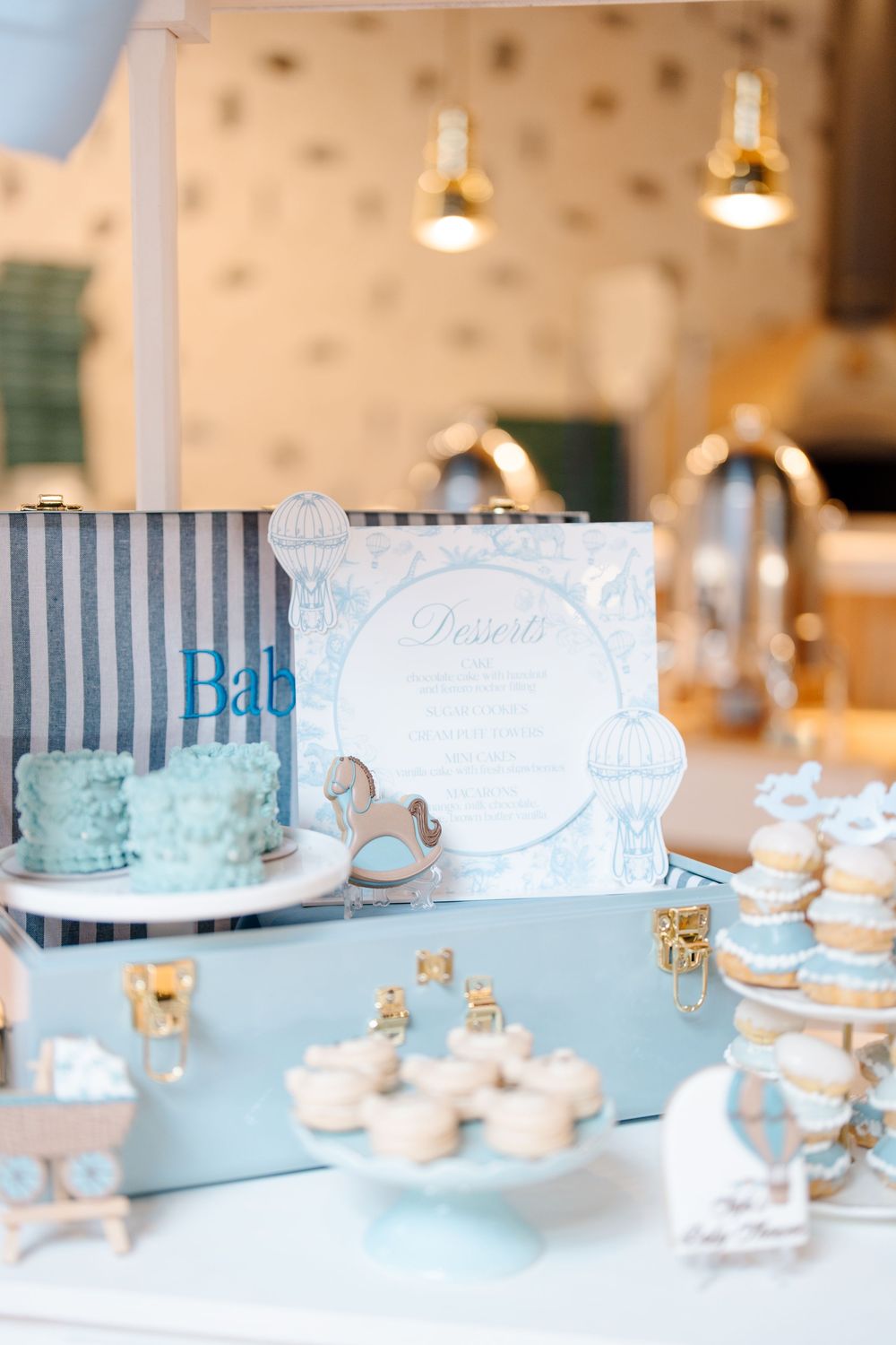 Blue baby shower dessert table with mini cakes, cupcakes, macarons, and decorative signage.