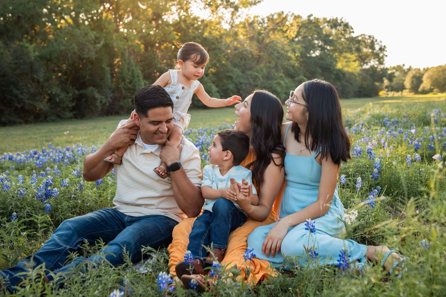 Group enjoying a warm sunset in a field of bluebonnets during golden hour Houston, Texas during a Bluebonnet Mini Session.