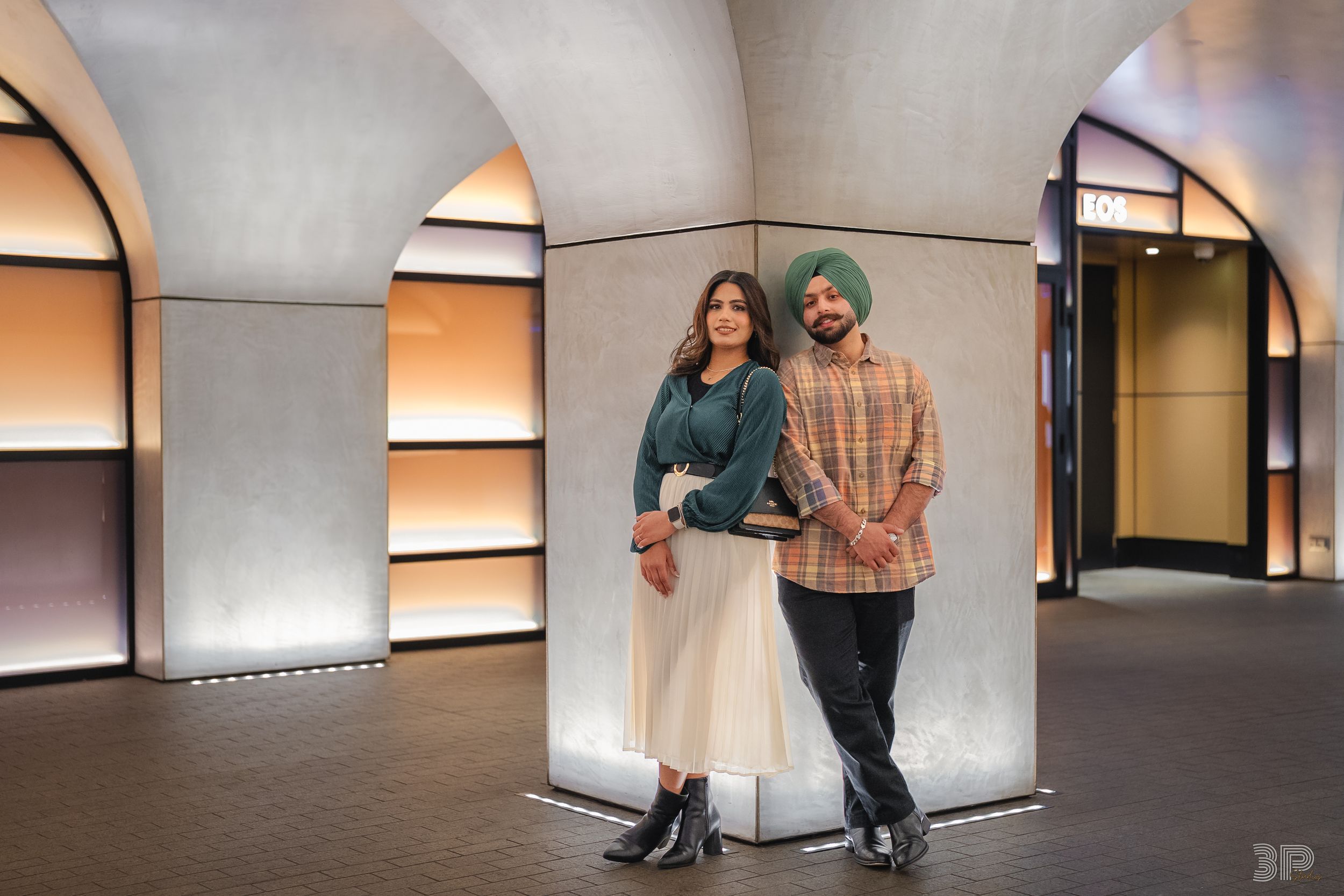 Two people lean against a wall in a modern interior space with arched illuminated alcoves.