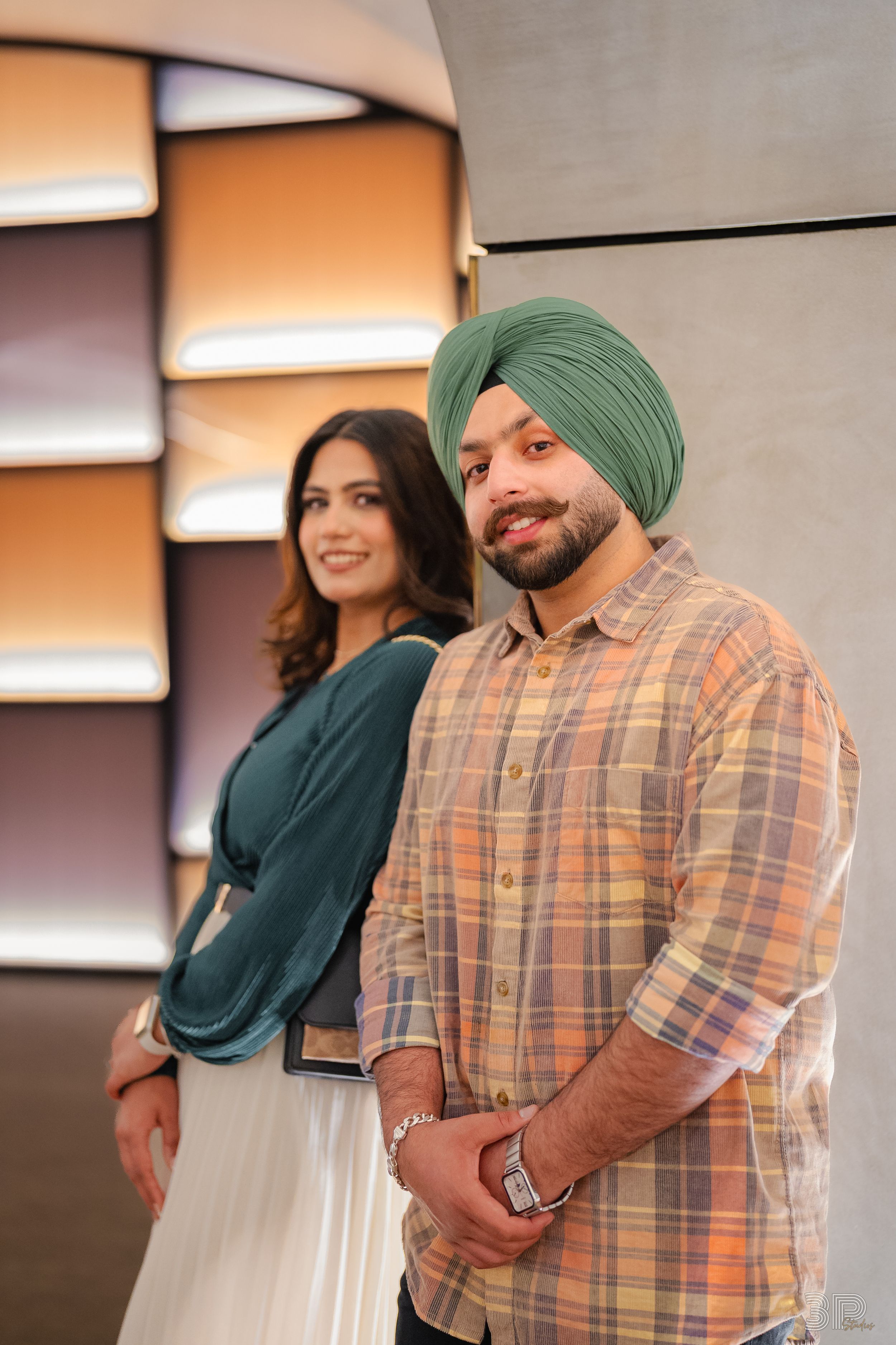 A couple in casual attire share a warm embrace and laugh together in an indoor setting.