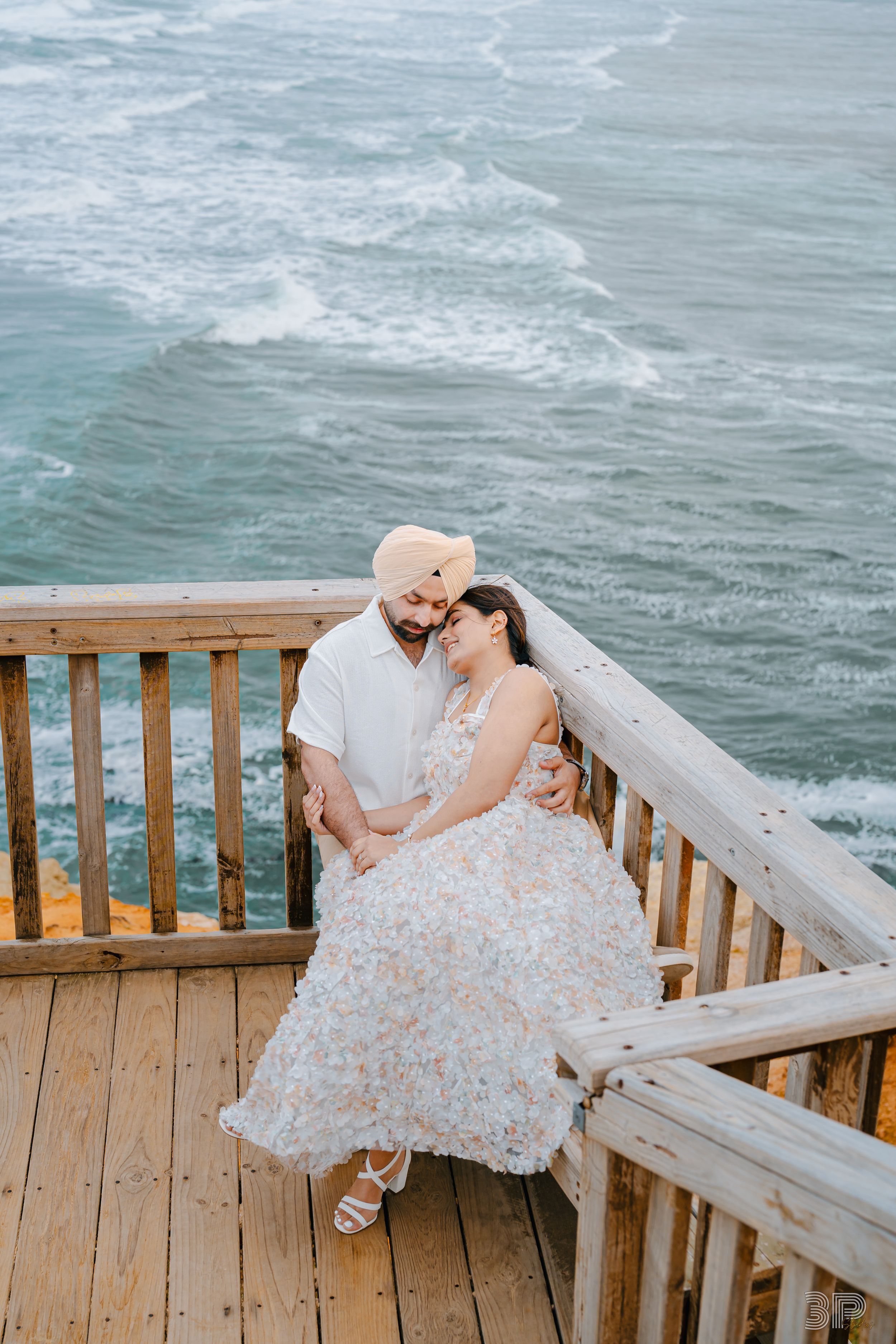 A couple shares a romantic moment on a wooden deck overlooking the ocean waves.