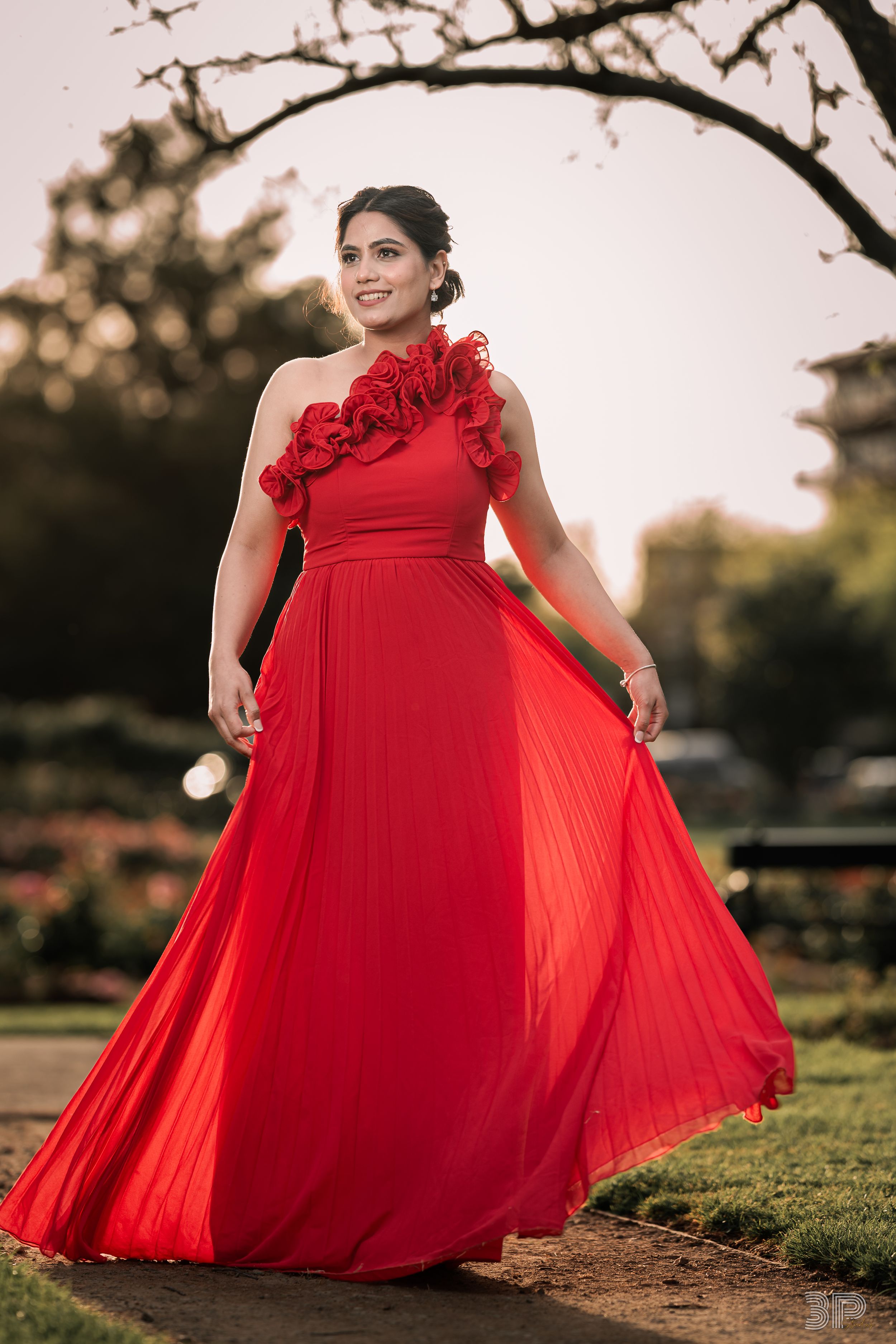 A flowing red formal dress with ruffled details twirls gracefully in an outdoor garden setting at sunset.