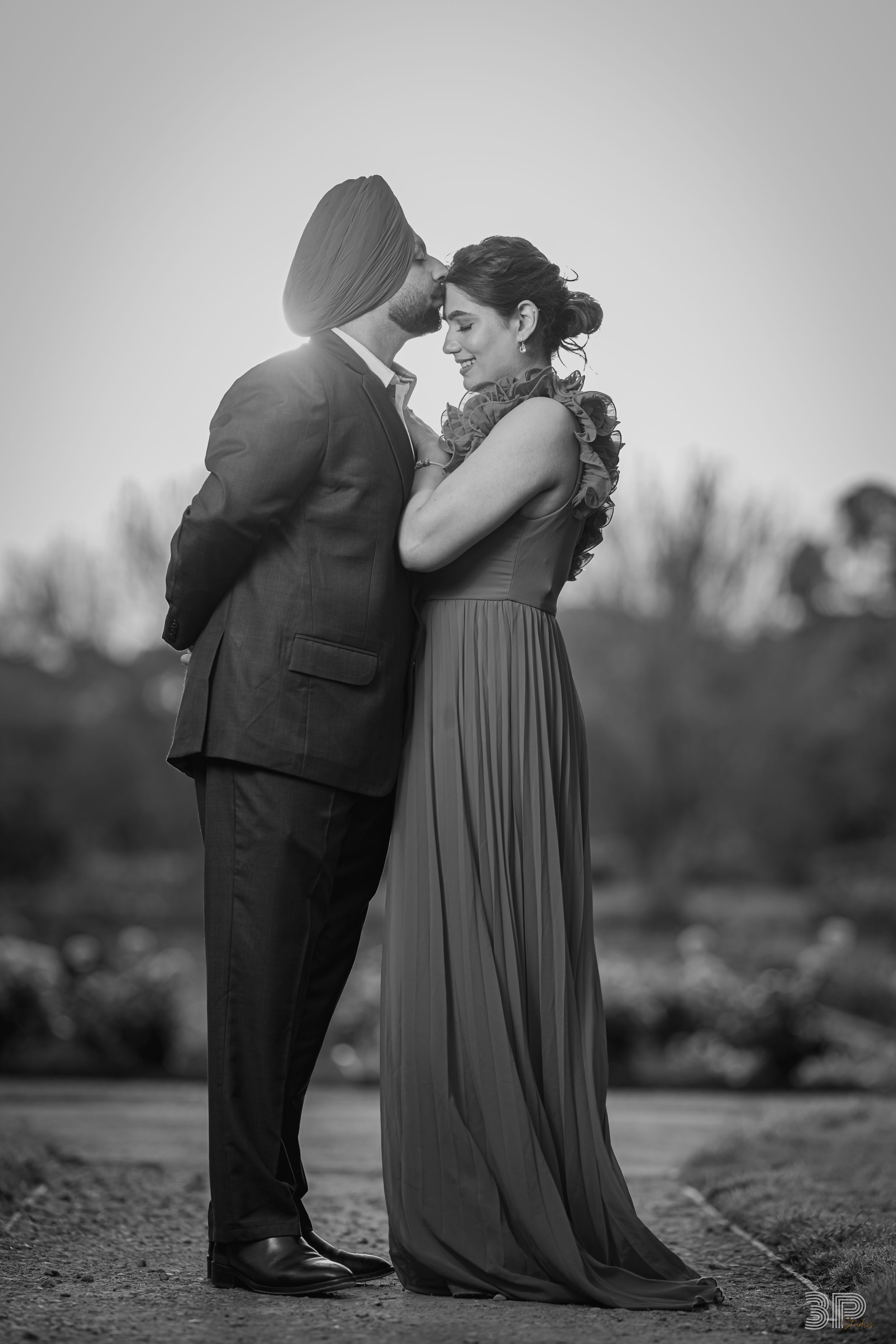 A black and white romantic portrait of a couple embracing outdoors in formal attire.