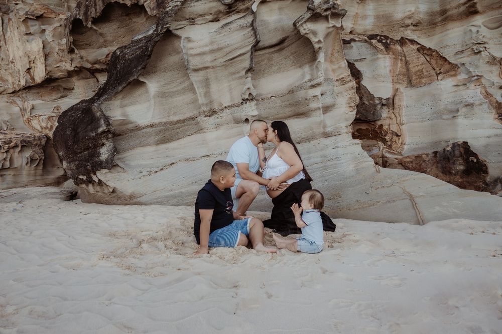Family sitting for a central coast maternity photo session infront of a rocky beach cave with natural stone formations.