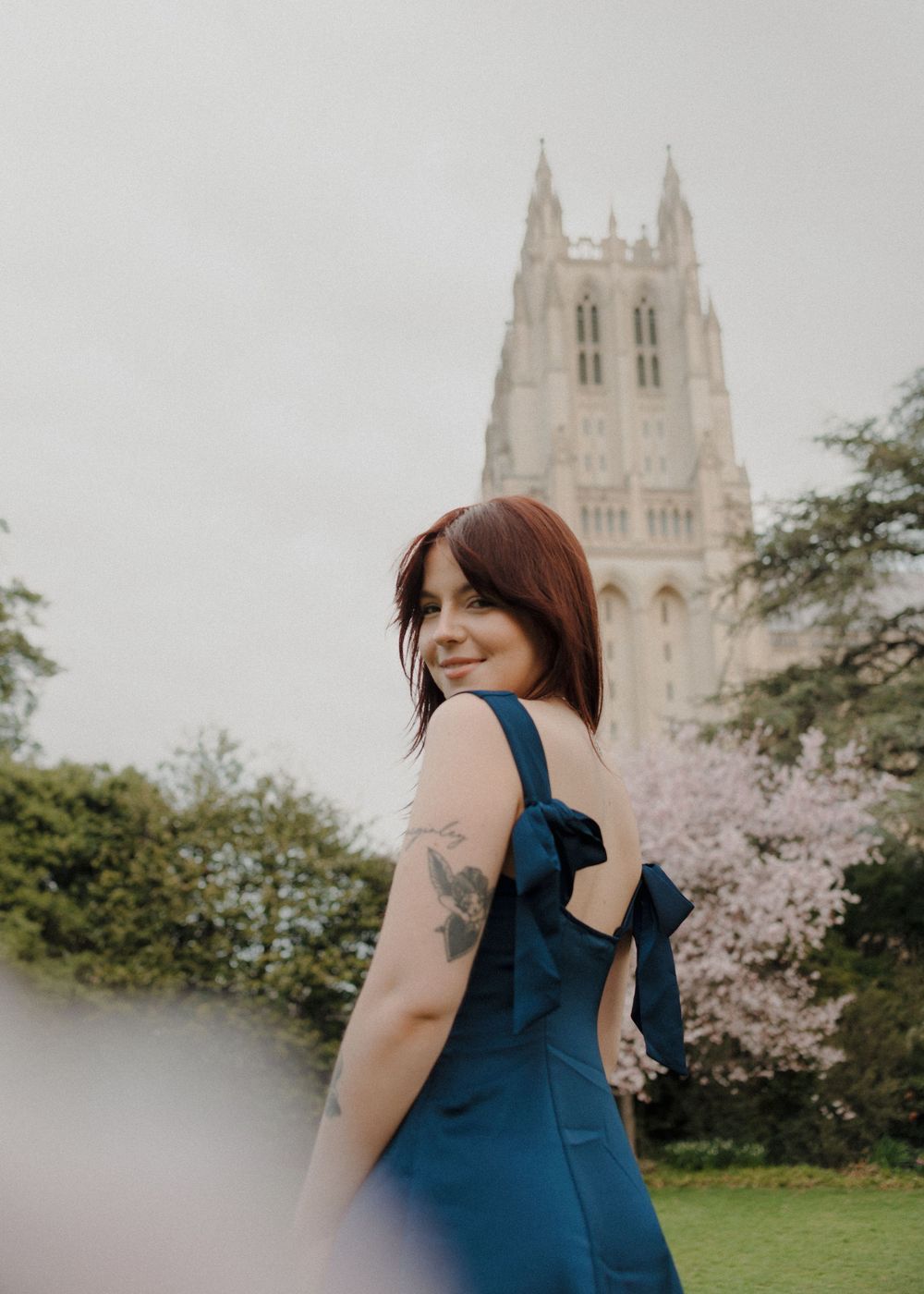 A scenic graduation photo with a Gothic cathedral spire and blooming cherry trees in soft light.