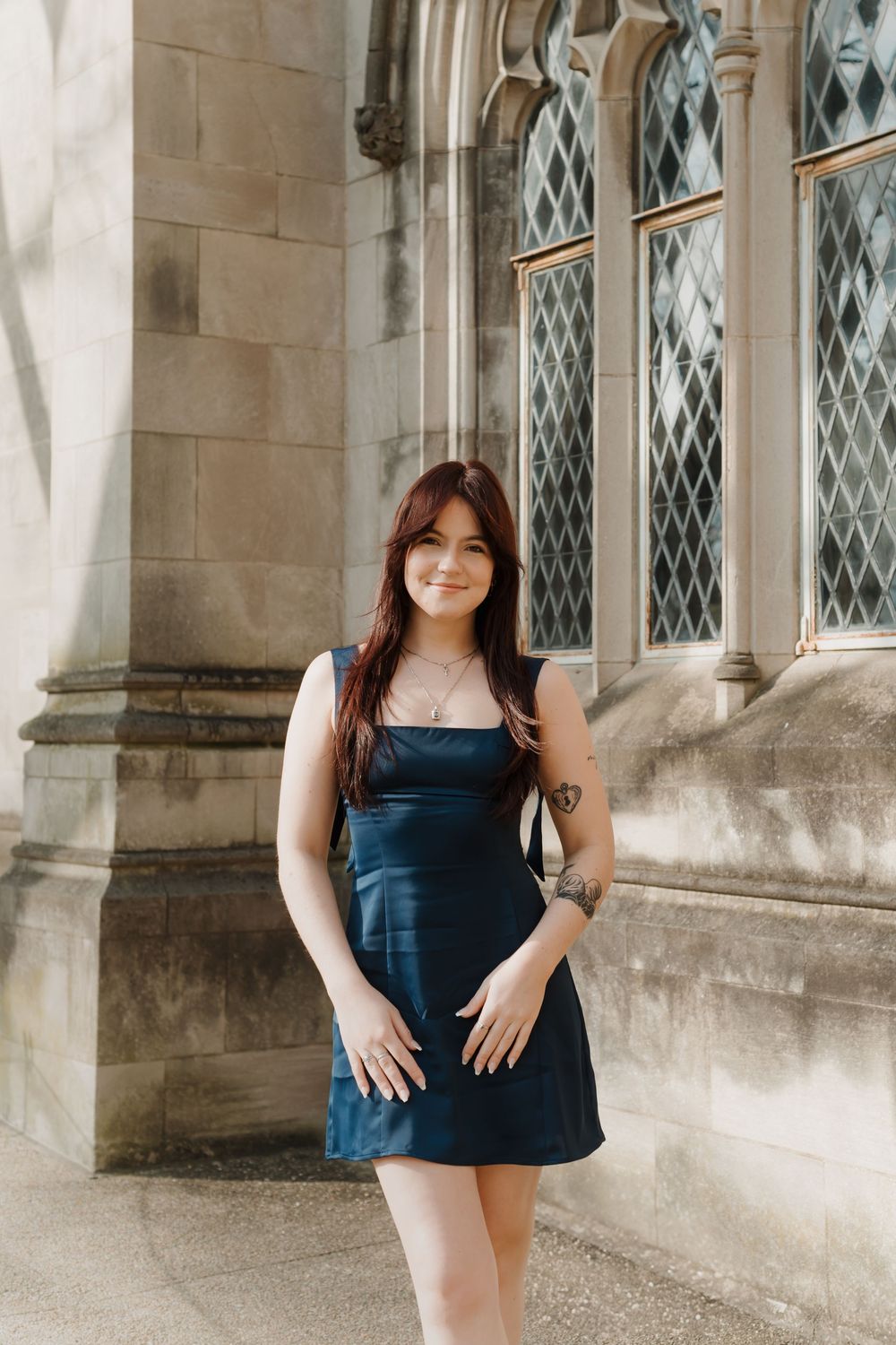 A navy blue dress stands out against light stone Gothic architecture with diamond-paned windows.