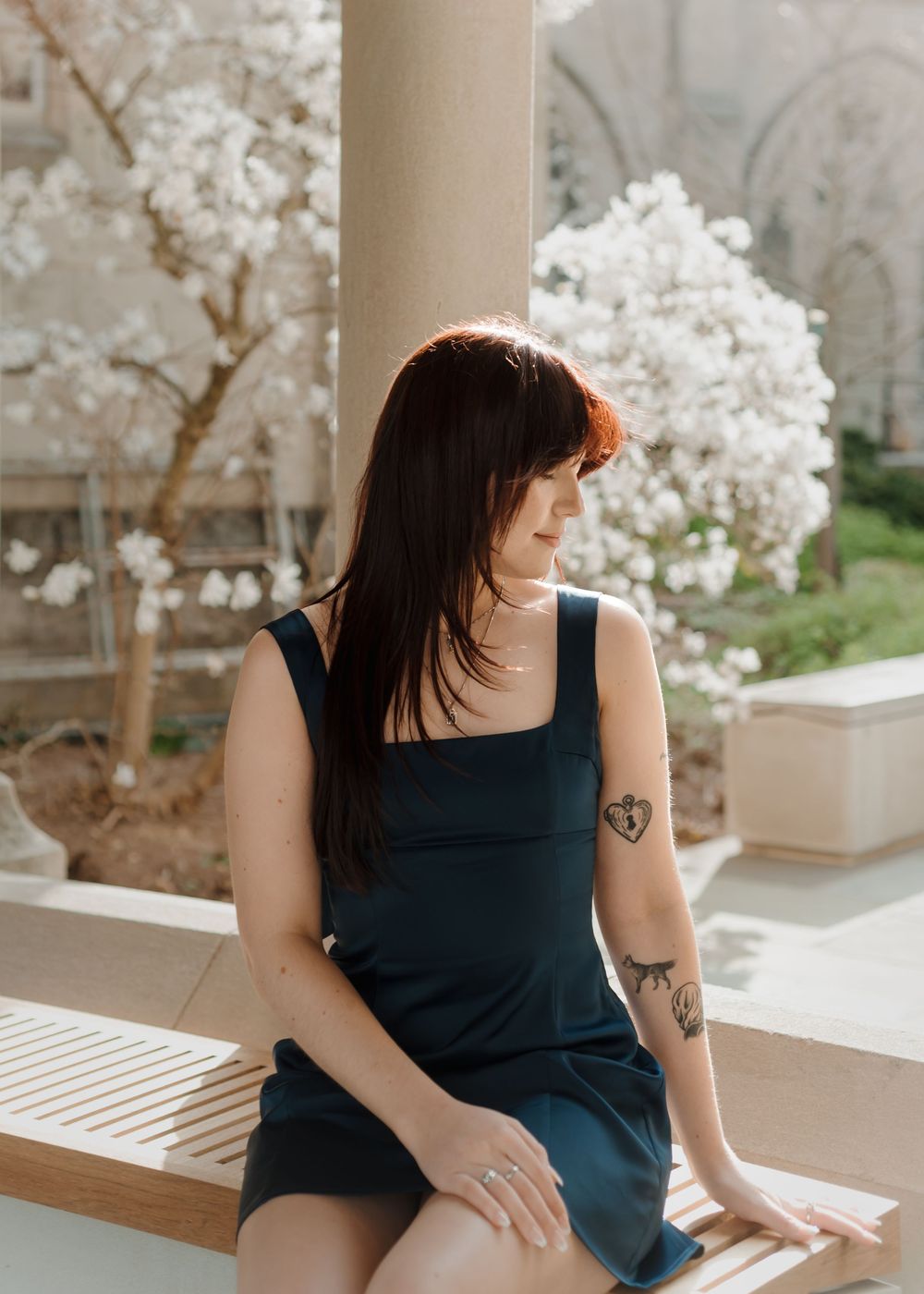 A casual portrait against white columns and cherry blossoms showing a black tank top and visible tattoos.