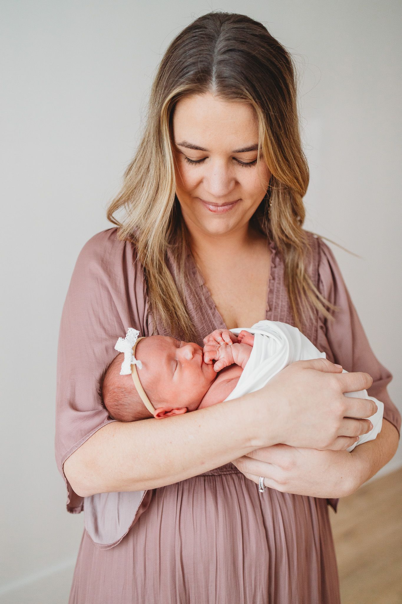 A mother in a dusty rose dress cradles and gazes lovingly at her newborn baby in a series of tender portraits.
