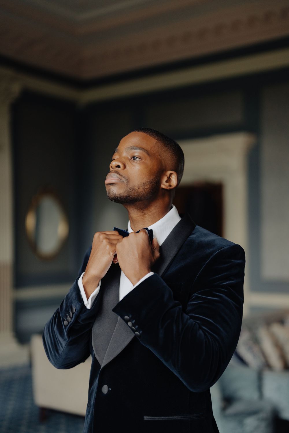 Person in formal black suit adjusting tie while looking upward in dramatic lighting.