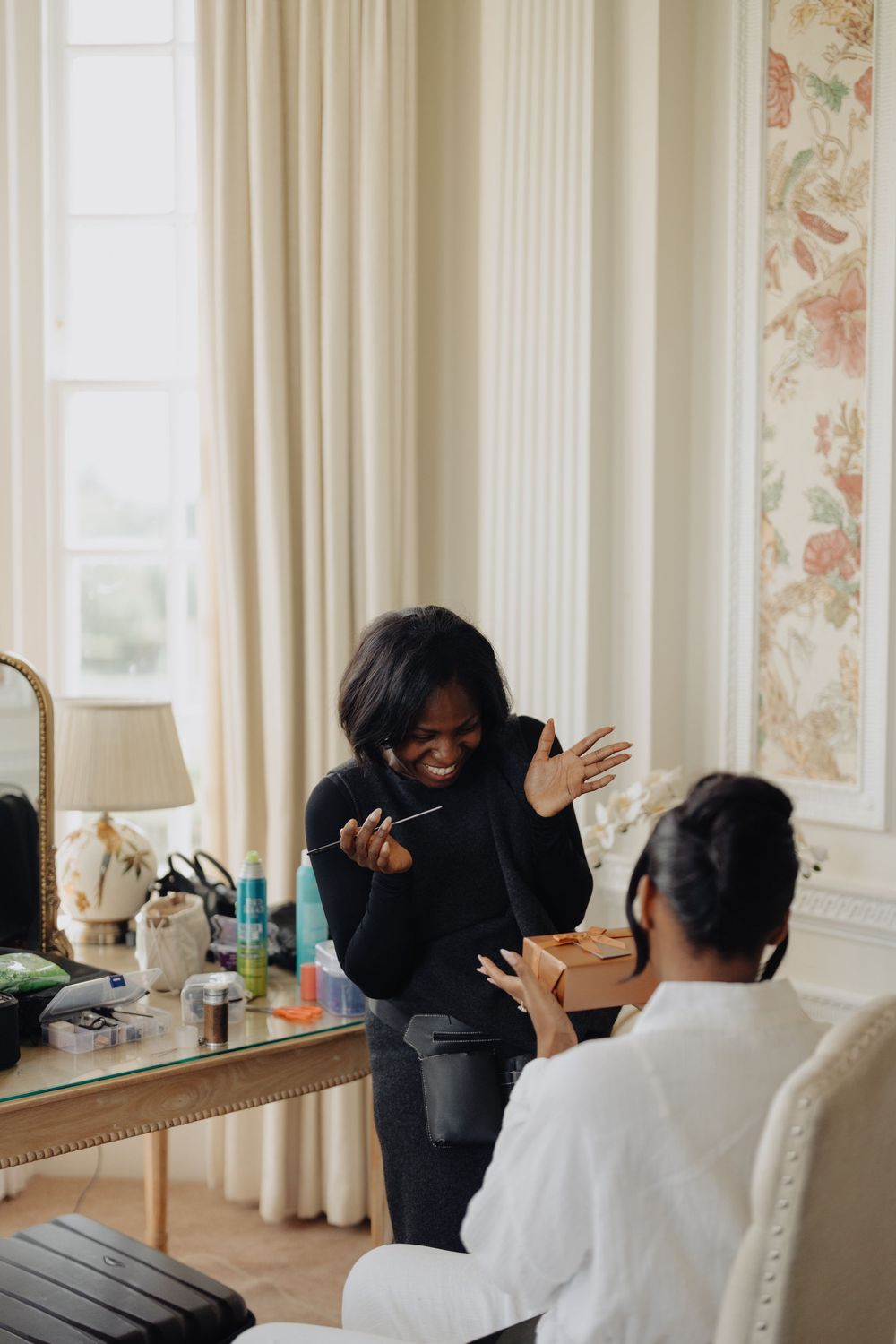 Two people share an animated moment while getting ready in an elegant room with floral wallpaper.