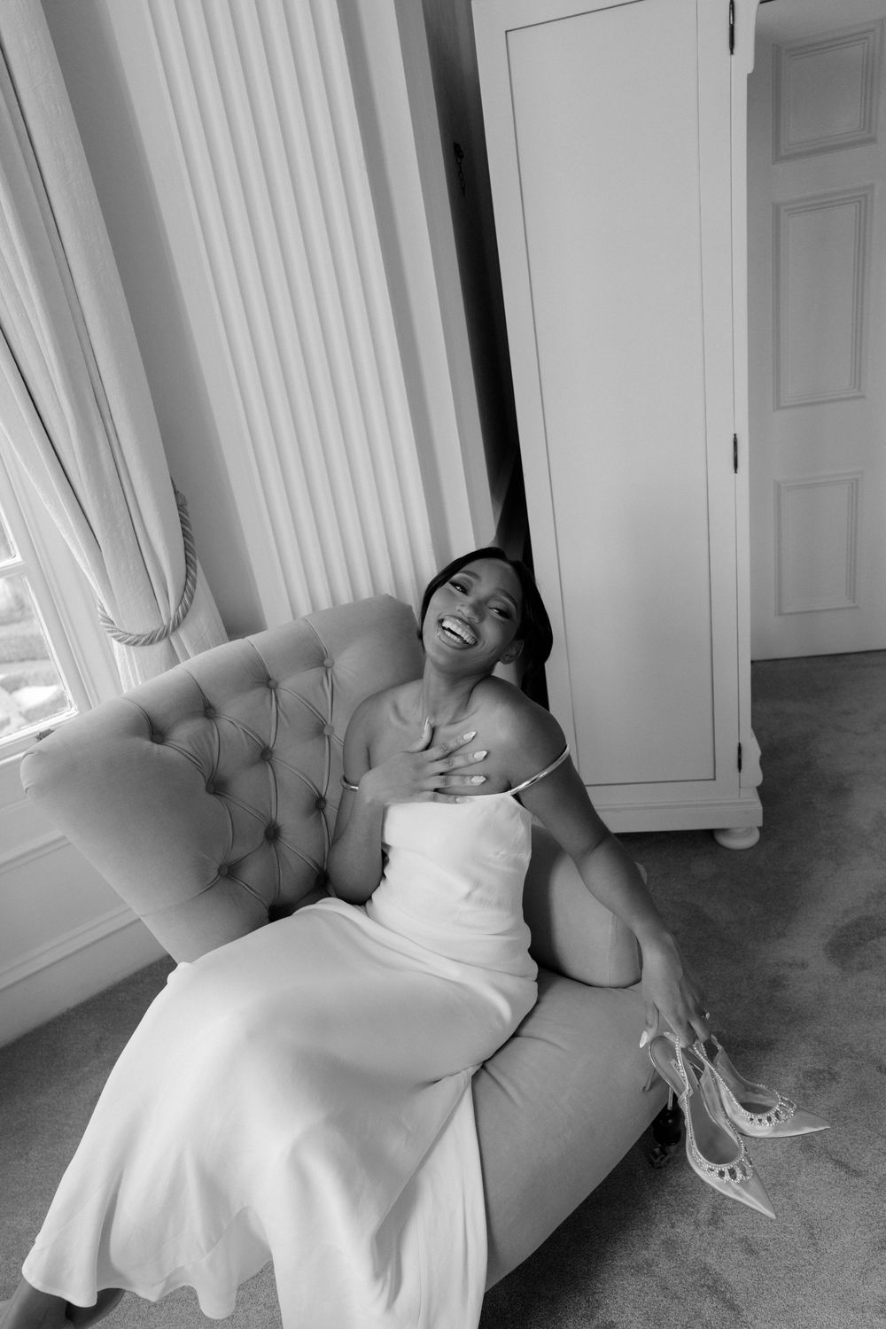 Candid bridal portrait on tufted chair in natural window light.