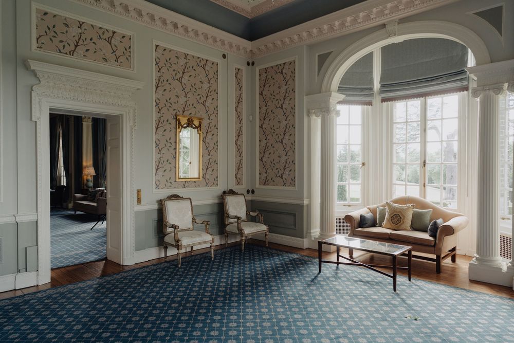 Elegant interior room with ornate wallpaper, crown molding and large windows letting in natural light.