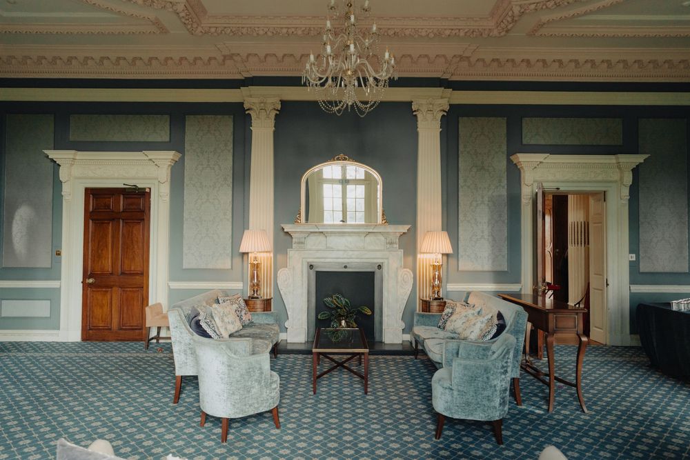 Elegant blue room with period furniture, fireplace and chandelier in historic mansion.