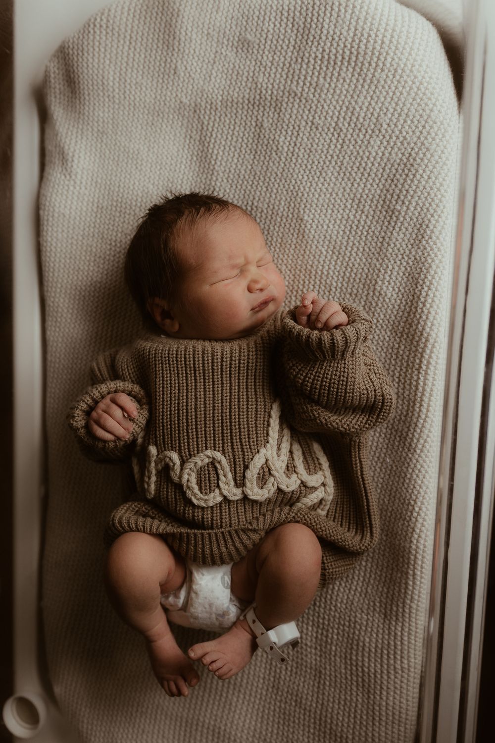 Newborn baby sleeping peacefully on soft beige knit blanket in artistic photo series.