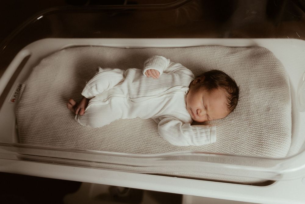 A sleeping newborn baby wearing white clothing lies peacefully on a gray changing pad.