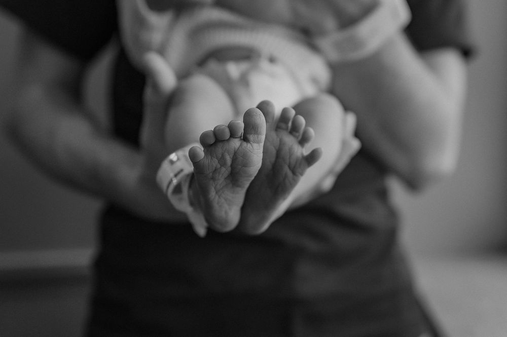 Black and white photo showing hands gently holding a small newborn baby's feet in close-up detail.