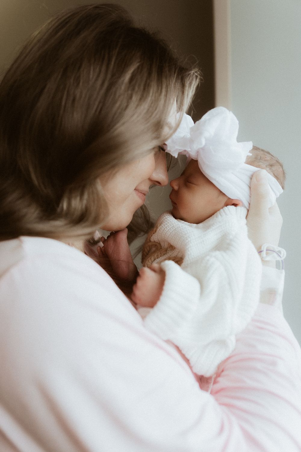 Tender moment between parent and baby dressed in white against light background.