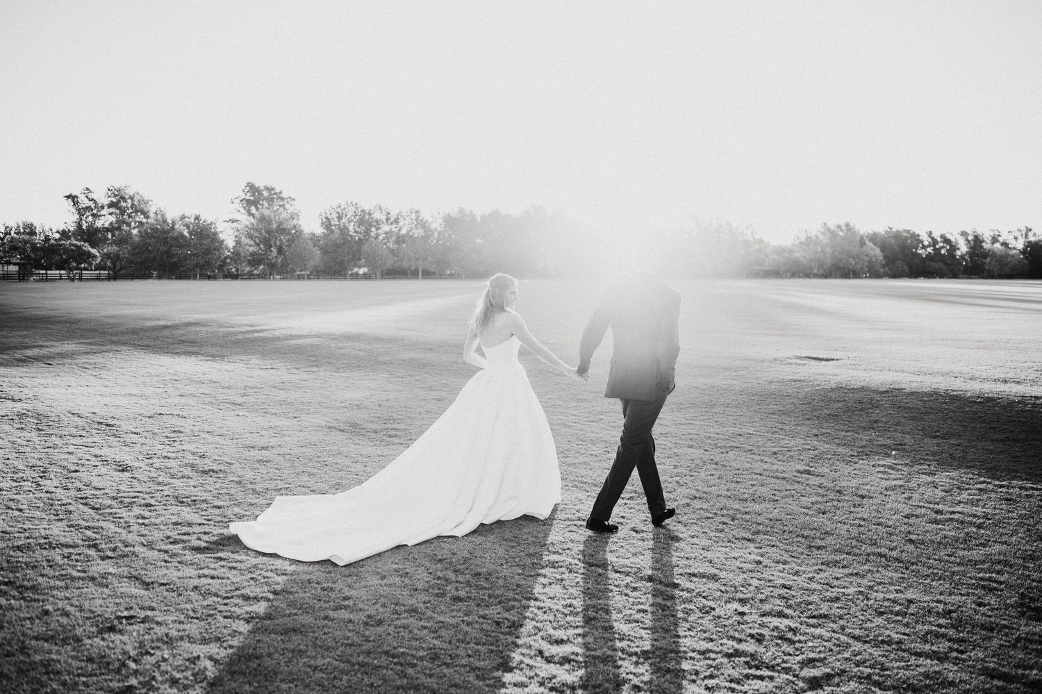 Silhouetted figures in flowing dress and suit walking across misty field at golden hour.