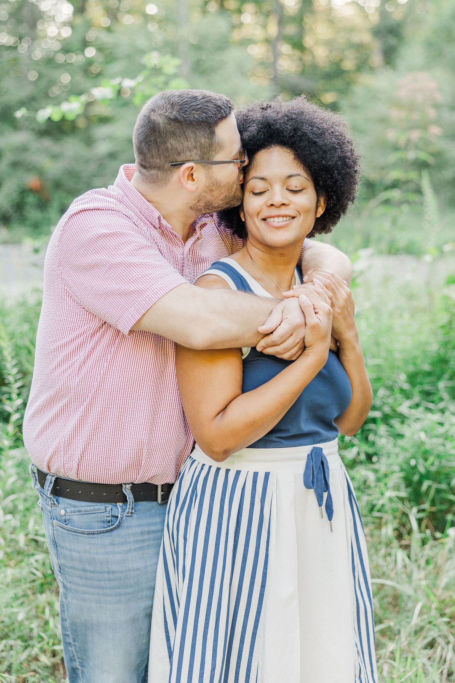 Intimate moment between couple embracing in sunlit forest clearing. Kristyn Romell Photography.