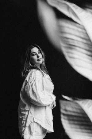 Artistic black and white portrait showing figure in white flowing top against dark background with dramatic shadows.
