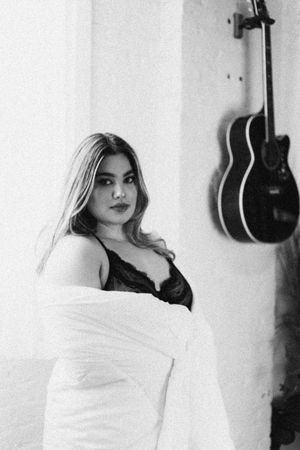 Monochrome indoor photoshoot featuring white clothing against wall with guitars displayed.