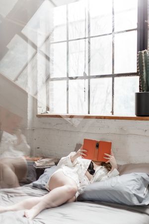 Bright sunlit bedroom interior with person reading book on white bedding.