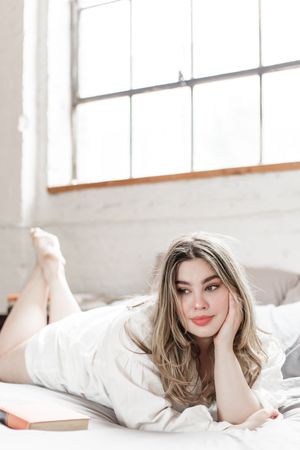 Lifestyle portrait of someone relaxing on white bedding in natural window light.