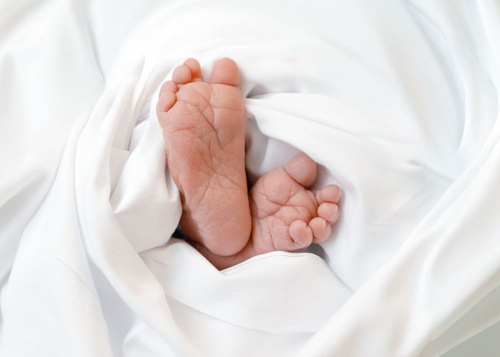 Tiny newborn baby feet resting on soft white fabric in a gentle and intimate close-up shot.