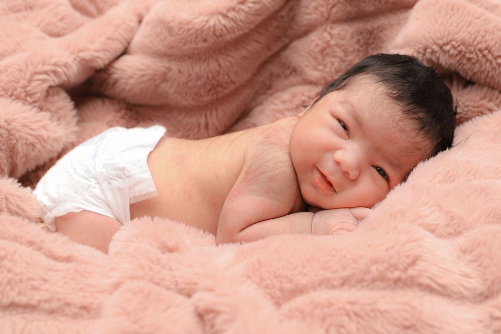 A peaceful sleeping newborn baby wearing a diaper nestles in soft pink blankets.