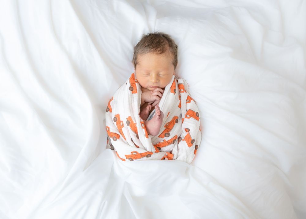 A sleeping baby in white bedding wearing orange and white patterned pajamas.