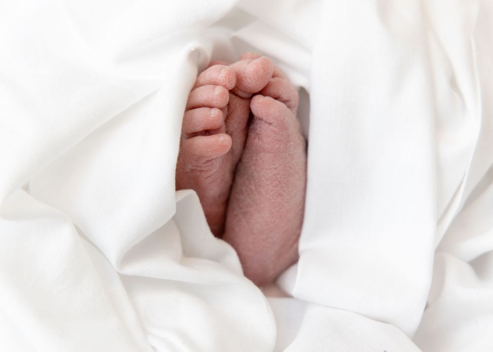 A newborn baby's tiny feet wrapped in soft white blankets against a light background.