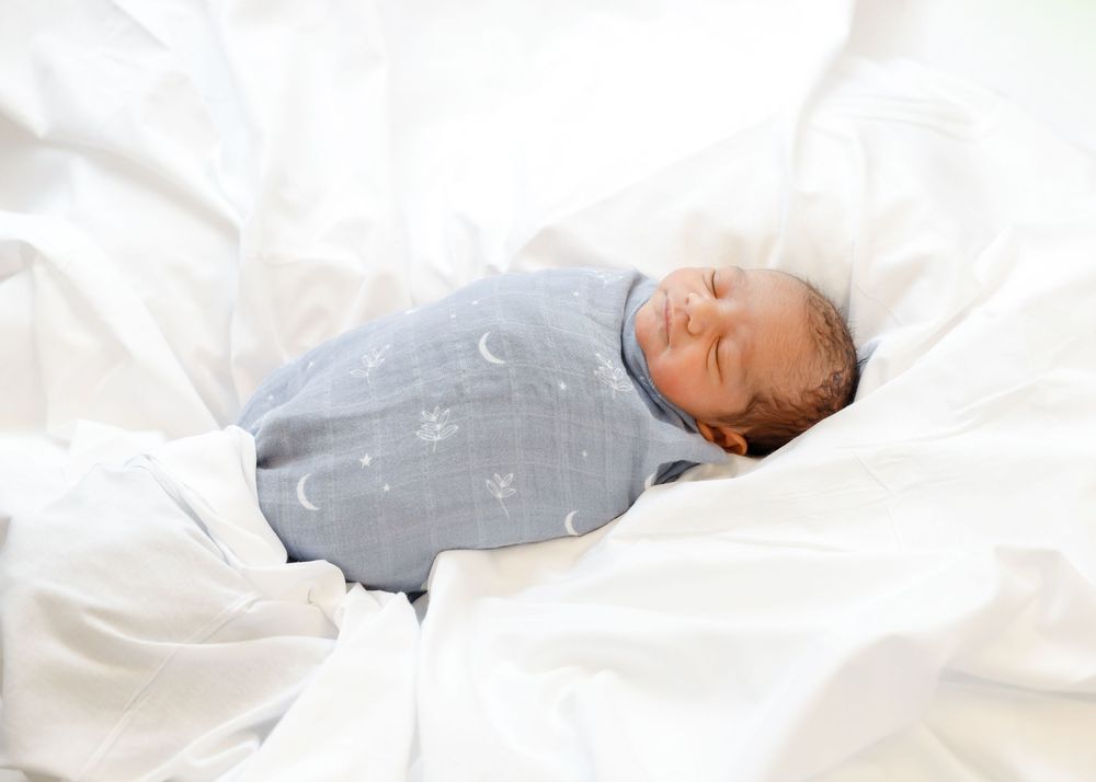 A sleeping baby wearing a gray onesie lies peacefully on white bedding.