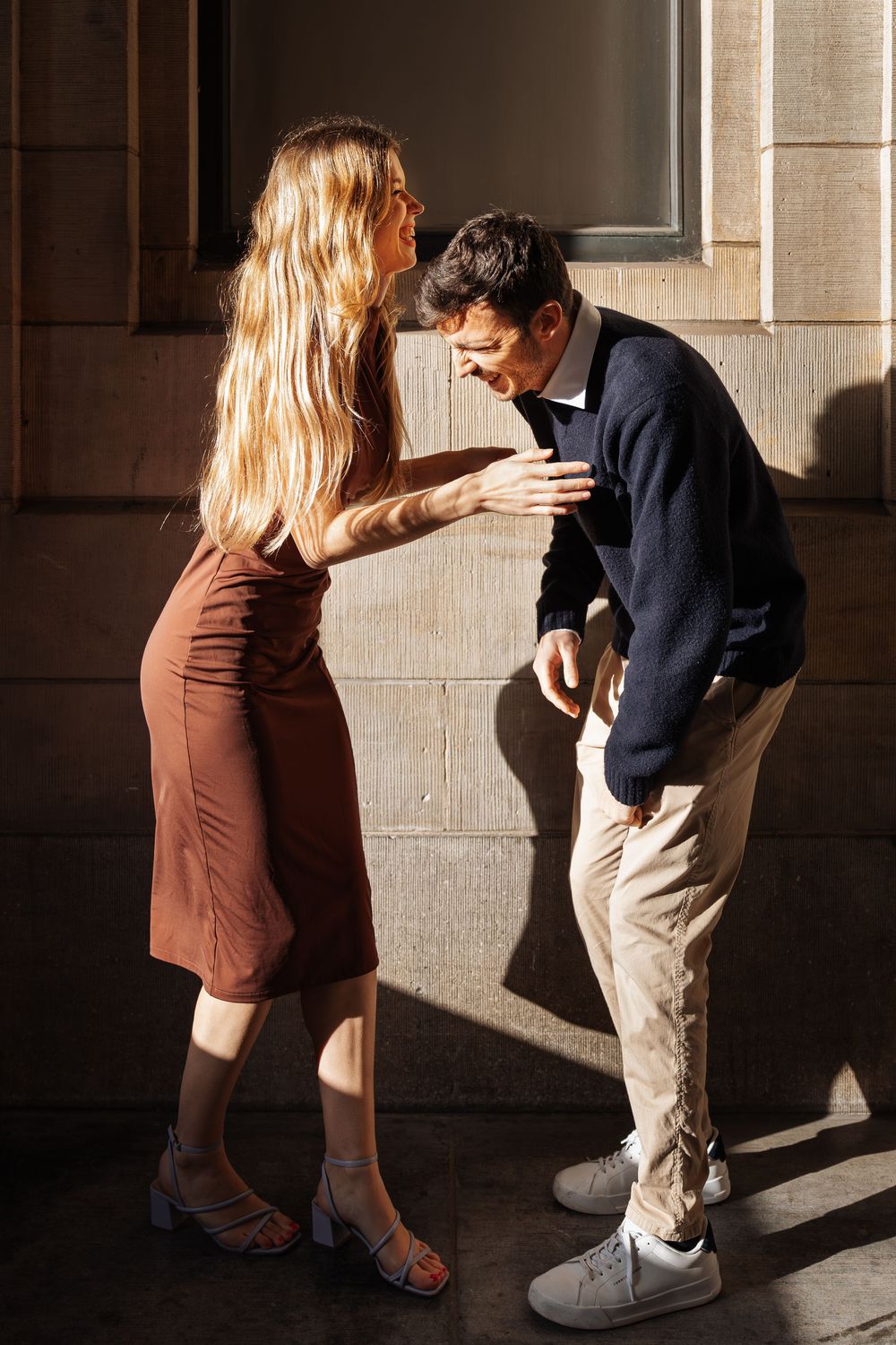 A couple in contrasting outfits dances playfully in dramatic lighting.