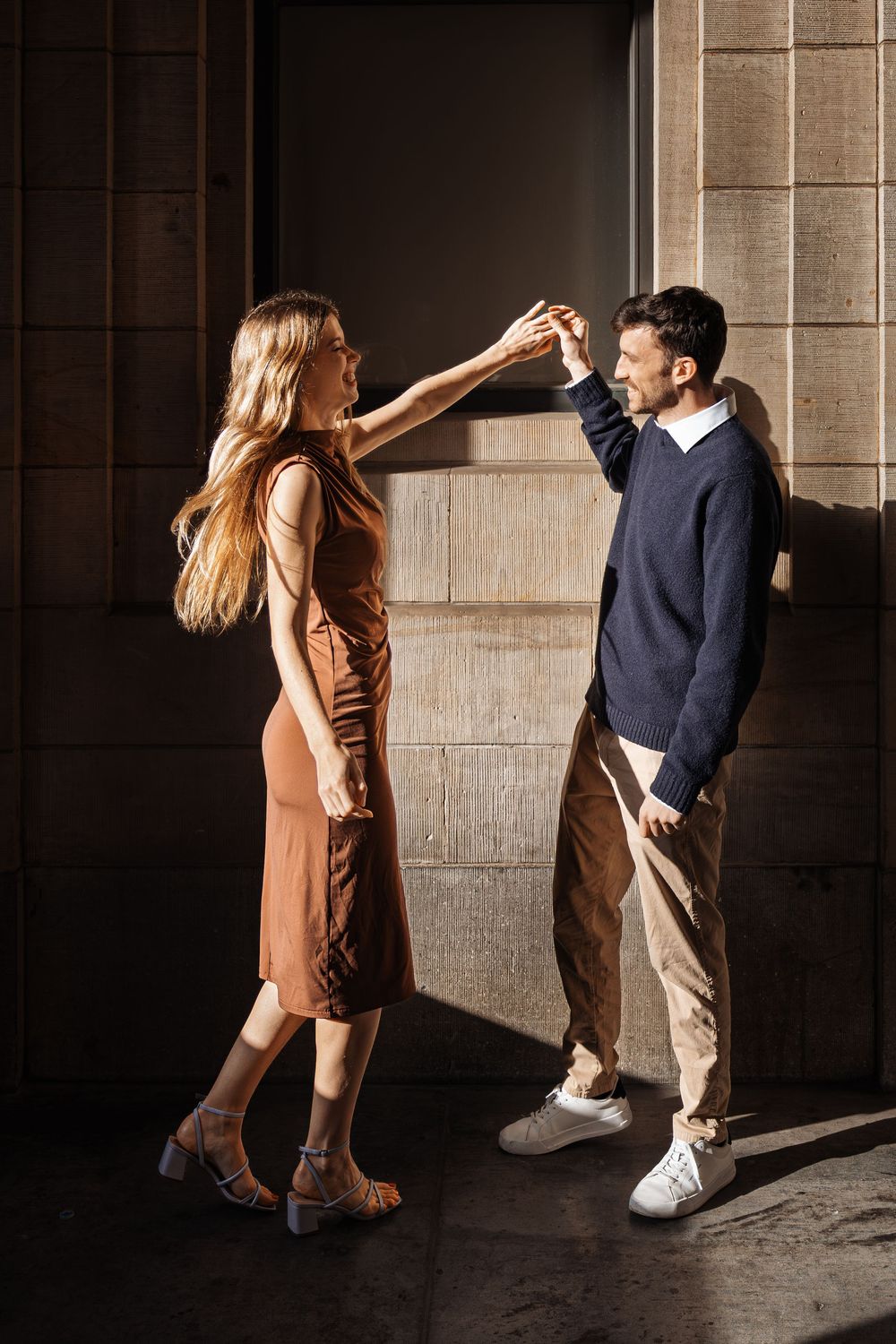 A couple in casual attire dances in a dramatic shadow-filled corridor.