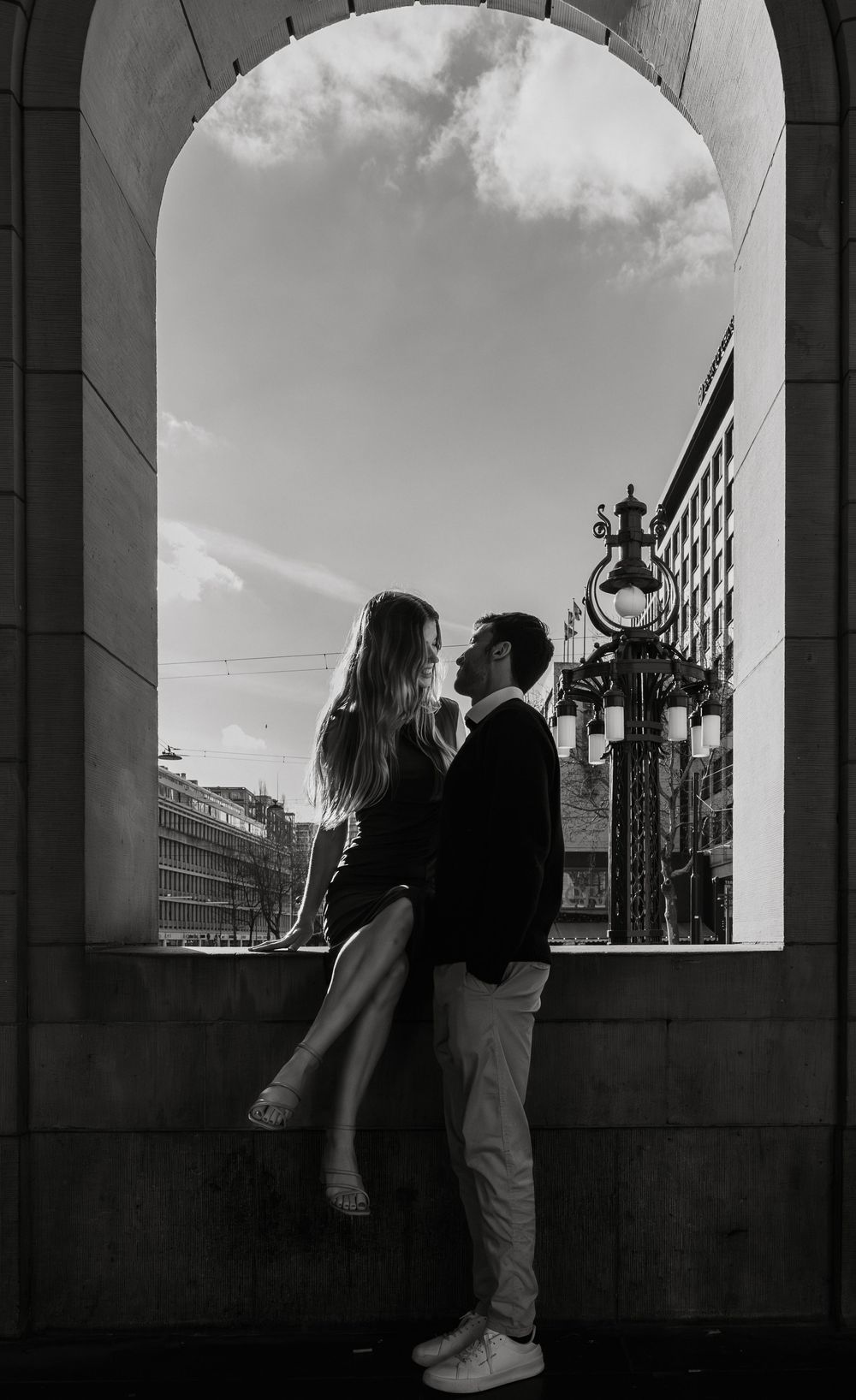 A silhouetted couple embraces against a bright sky through an arched window.